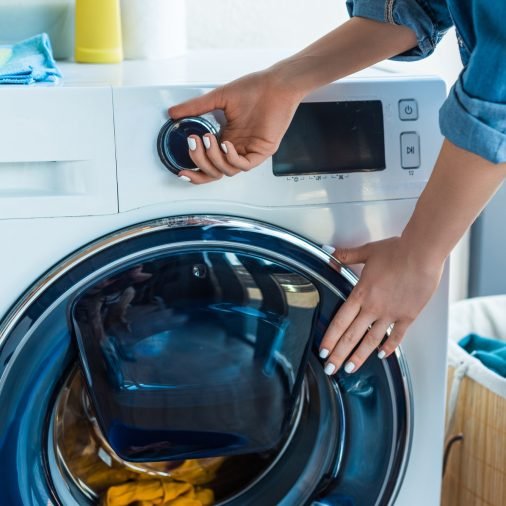 cropped shot of woman using washing machine at home